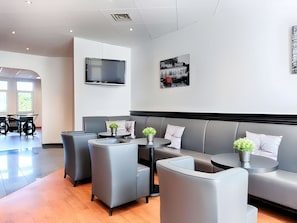 Un área de descanso moderna con sofás y sillones grises, un televisor de pantalla plana en la pared y una mesa con una planta en maceta.