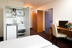 Habitación de hotel con cama, escritorio con silla, televisor, microondas y pequeña kitchenette.