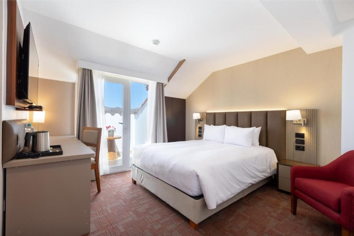 Une chambre d’hôtel avec un lit, un bureau, une télévision et une chaise rouge.