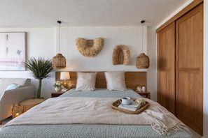 Een slaapkamer met een bed, nachtkastjes, een lamp, een houten kledingkast en een hartvormige decoratie aan de muur.