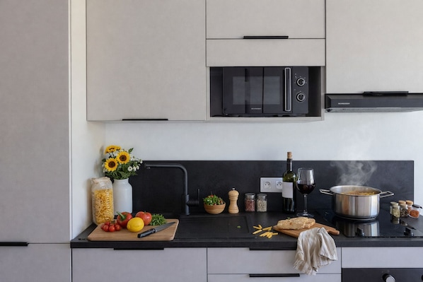 Een moderne keuken met een zwarte magnetron, een pan op het fornuis en diverse etenswaren op het aanrecht.