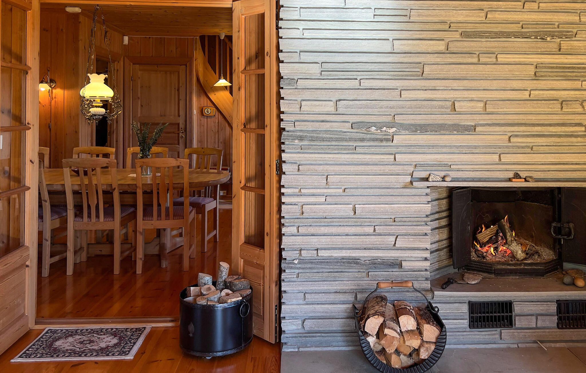 A wooden interior with a stone fireplace, dining area, and a fireplace mantel with logs.