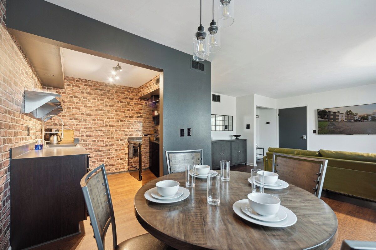 A modern kitchen with a brick wall, a dining area with a round table, and a green sofa.