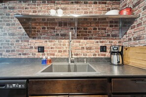 A kitchen with a brick wall, a stainless steel sink, and a coffee maker. - Fairlane #3 I 2 BR 1 BA (Lansing)
