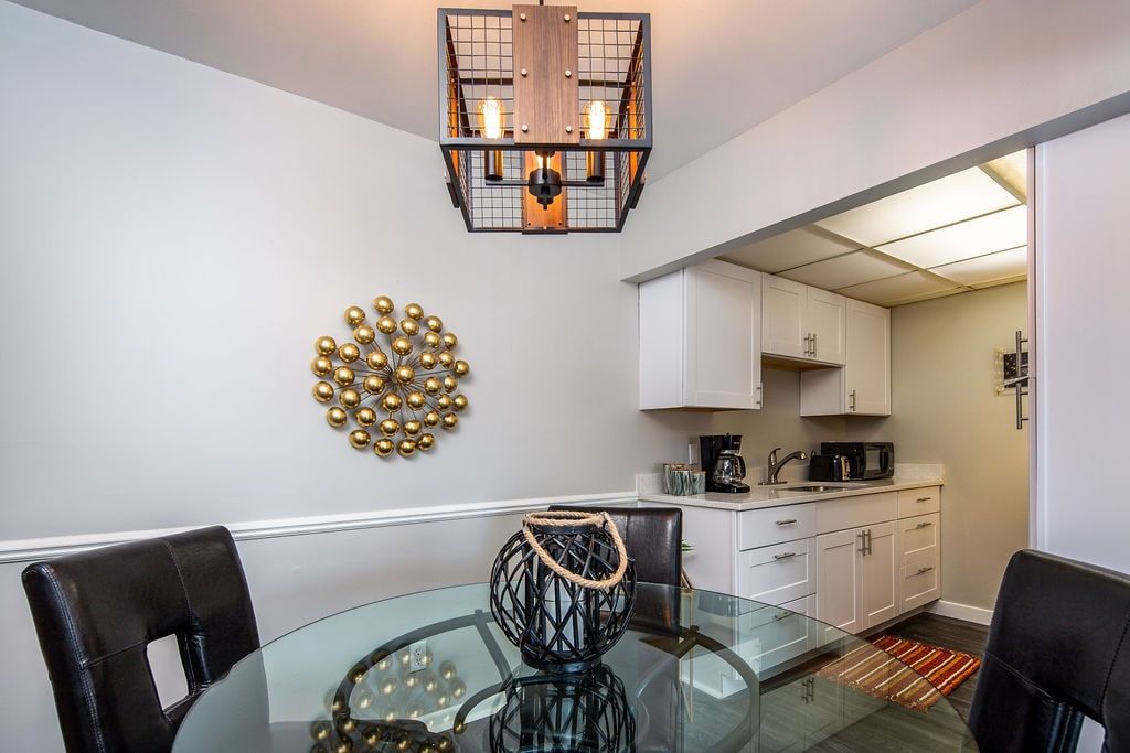 A modern kitchen with white cabinets, a glass dining table, and a unique wall decoration.