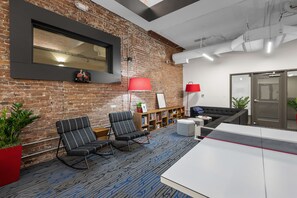 A modern office space with a brick wall, two black striped chairs, a red lamp, a bookshelf, and a white desk.