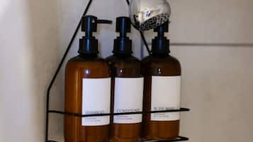 Un bagno con un soffione montato a parete e tre flaconi di shampoo, balsamo e detergente corpo su una mensola metallica.