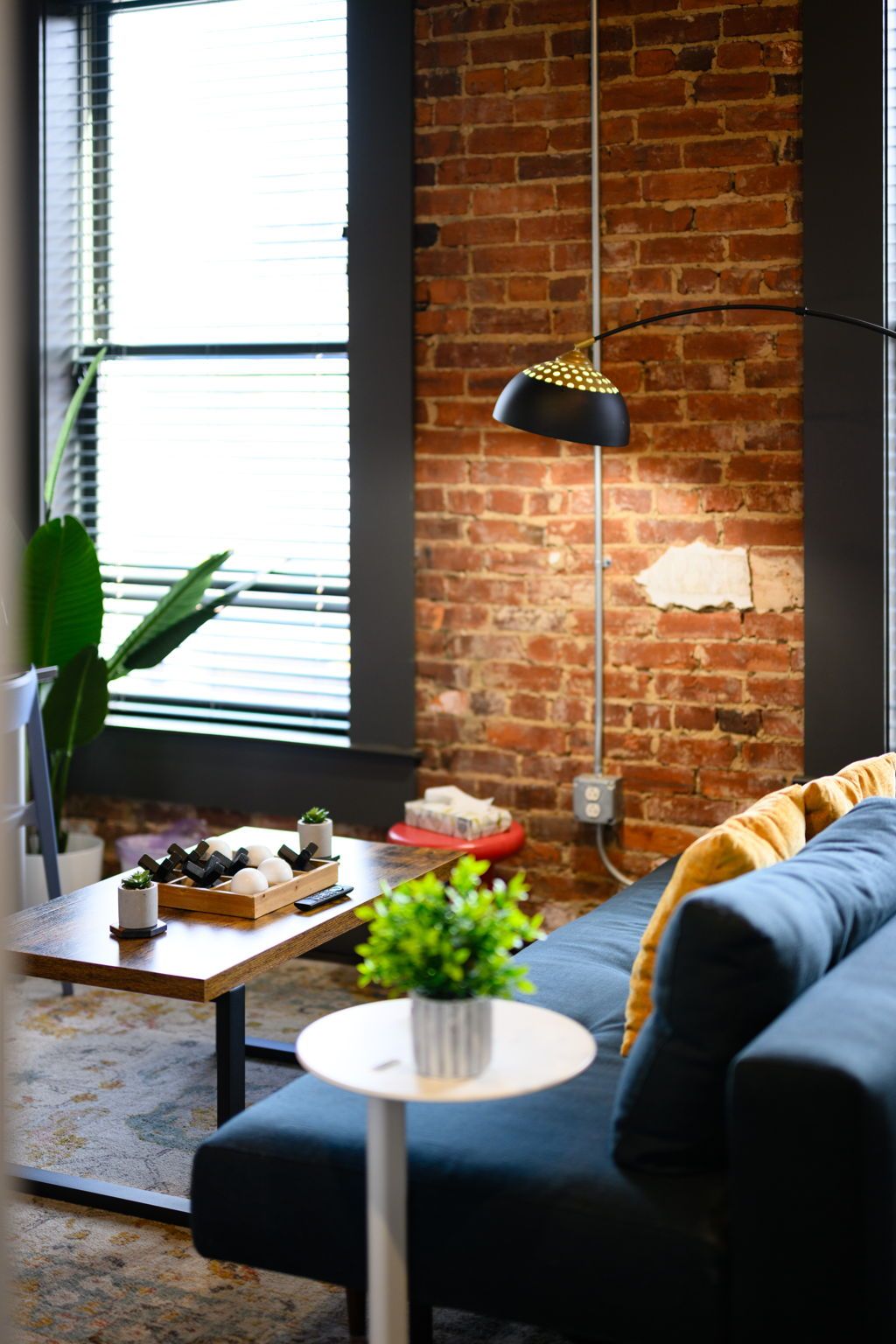A living room with a brick wall, a wooden coffee table, a black sofa, a small round table, and a hanging lamp.