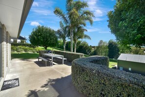 An outdoor patio with a table and benches, surrounded by well-maintained hedges and palm trees. - Country Cottage - cosy & private (Tauranga)