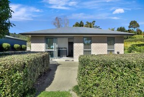 A modern two-story house with a paved driveway, a covered front porch, and a well-maintained garden. - Country Cottage - cosy & private (Tauranga)