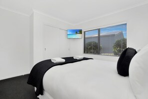 A hotel room with a bed, a television, and a window with blinds.