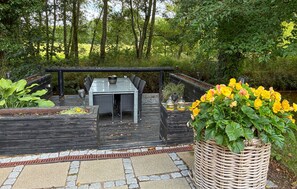 An outdoor dining area with a table and chairs, surrounded by greenery and a wooden deck. - Stunning home in Herning with WiFi (Herning)
