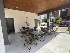 An outdoor patio area with tables and chairs, a fire extinguisher, and a view of parked cars and a building in the background. - CARIBBEAN CORNER (Cancún)
