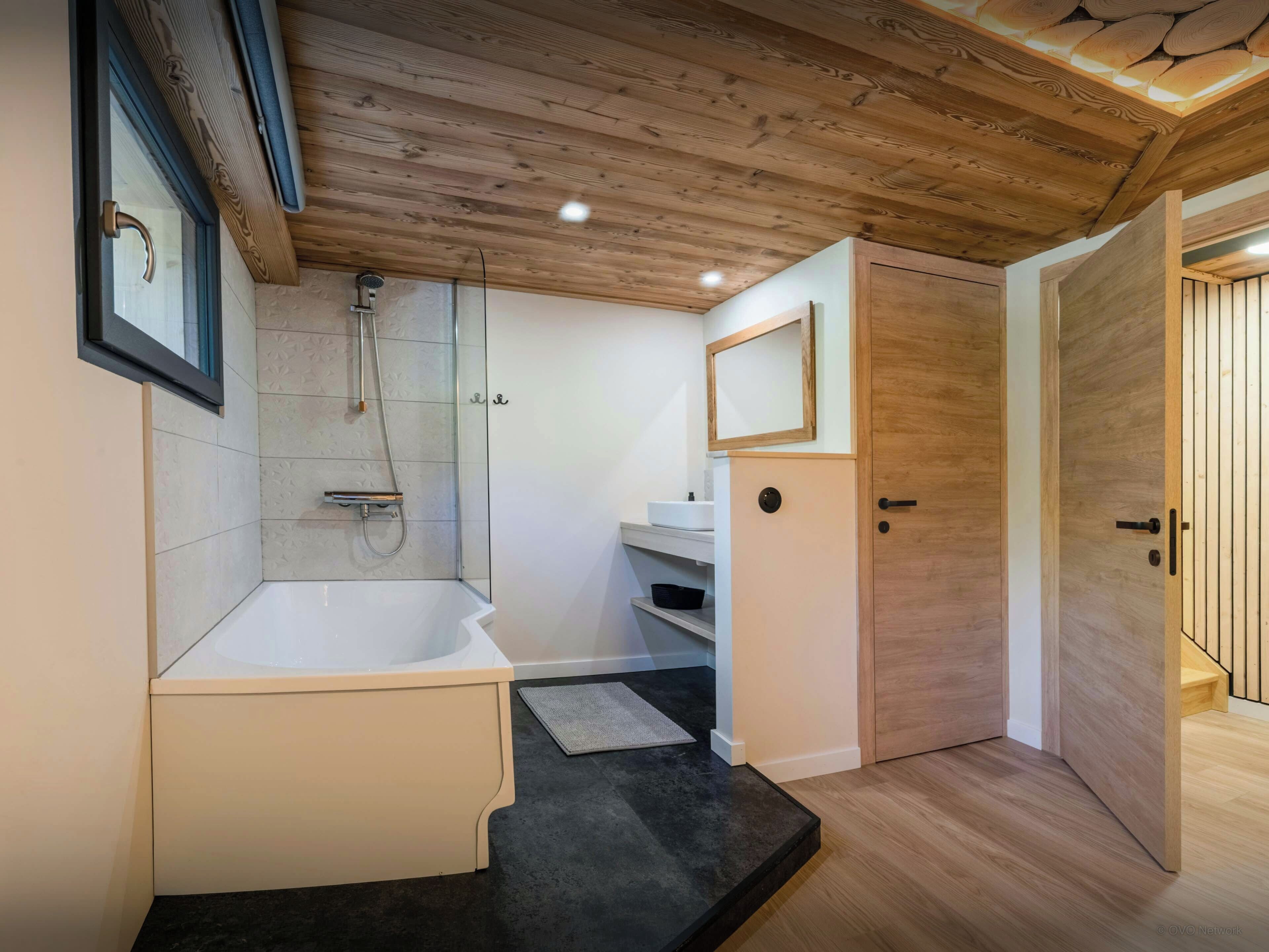 Een moderne badkamer met een bad, douche en een houten plafond.