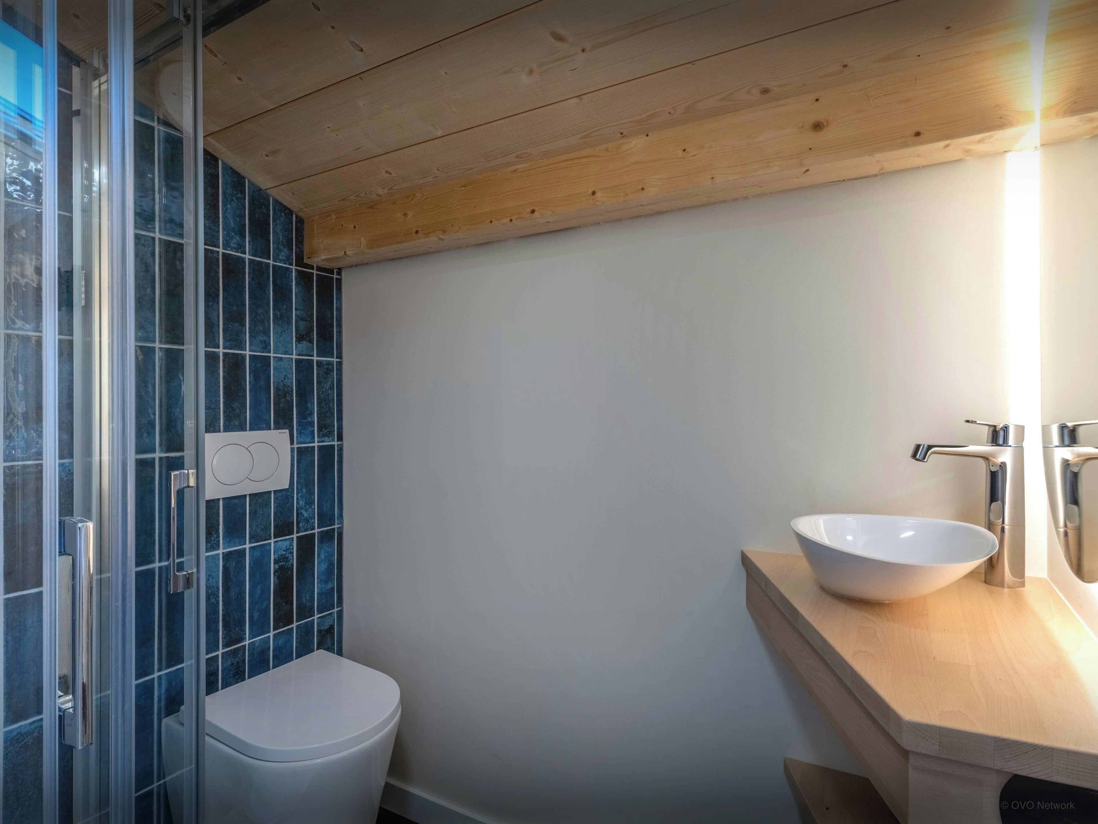 Une salle de bain avec des toilettes blanches, une douche en verre et un meuble-lavabo en bois avec un lavabo blanc.