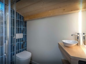 Ein Badezimmer mit Toilette, Duschkabine aus Glas und einem Holzwaschtisch mit weißem Becken.