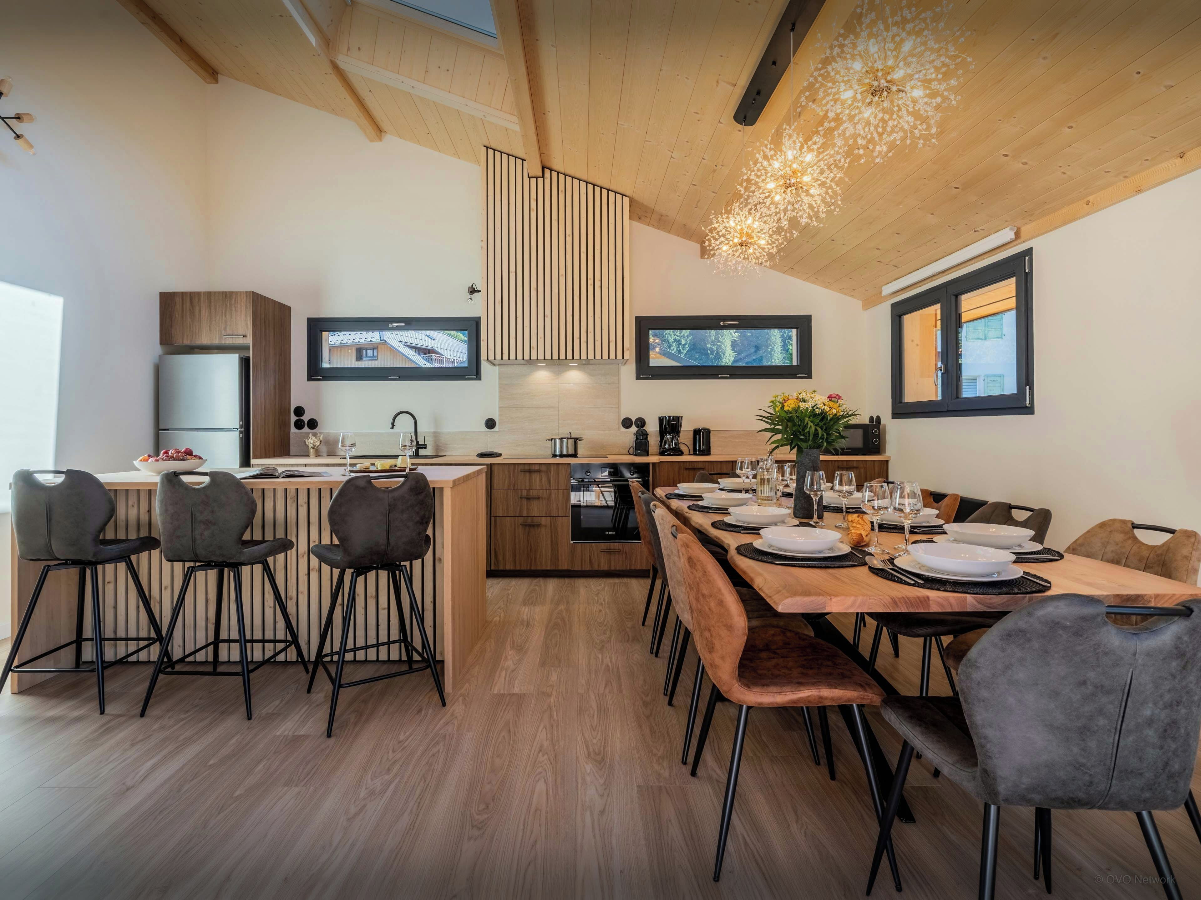 Une cuisine moderne avec un coin repas, un plafond en bois et des téléviseurs encastrés.
