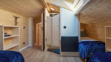 Une pièce chaleureuse aux murs en bois et dotée d’une lucarne, comprenant deux lits avec une literie bleue et une petite étagère.