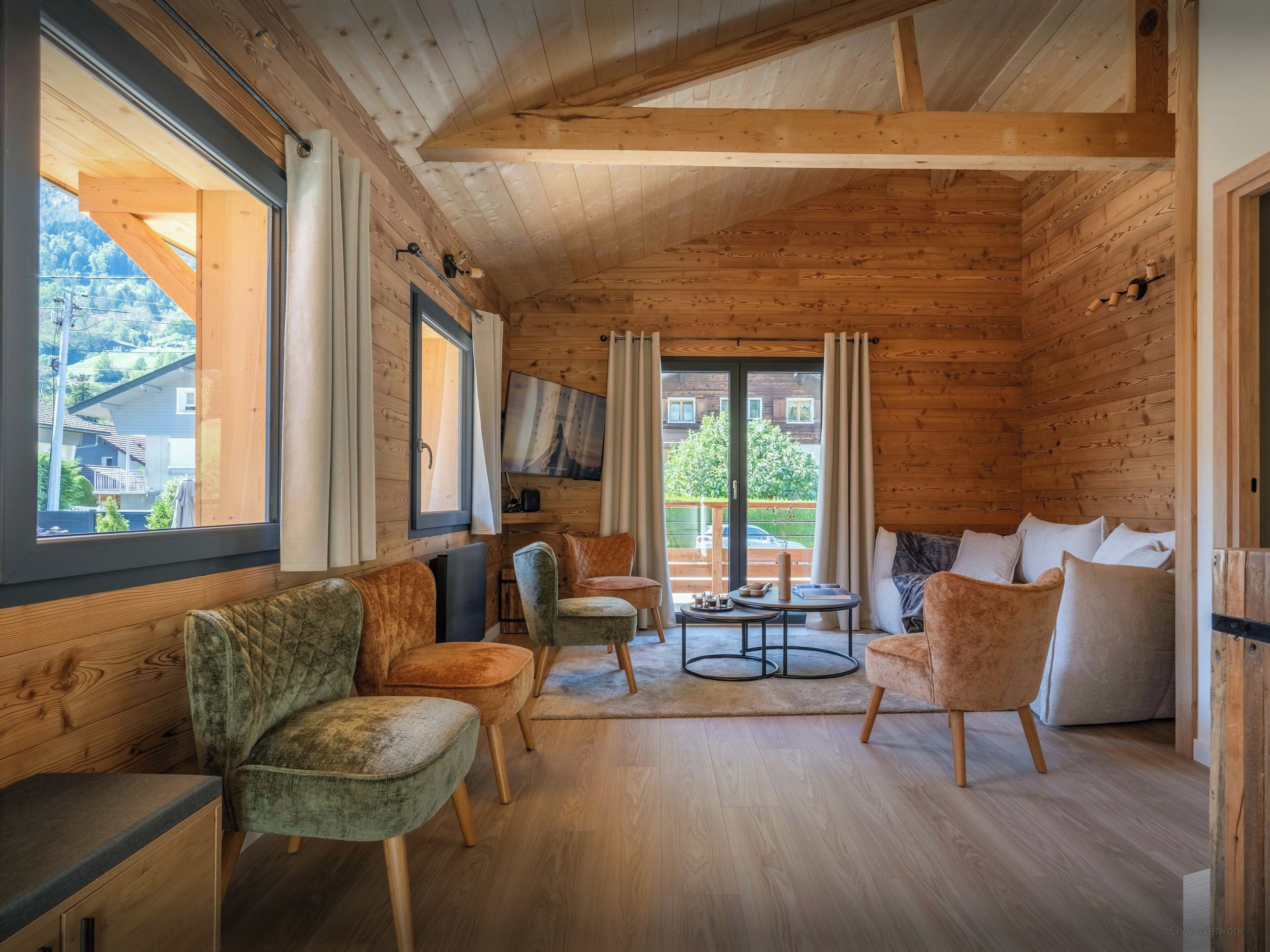 A cozy cabin interior with wooden walls, a sofa set, a television, and a view of the outside.