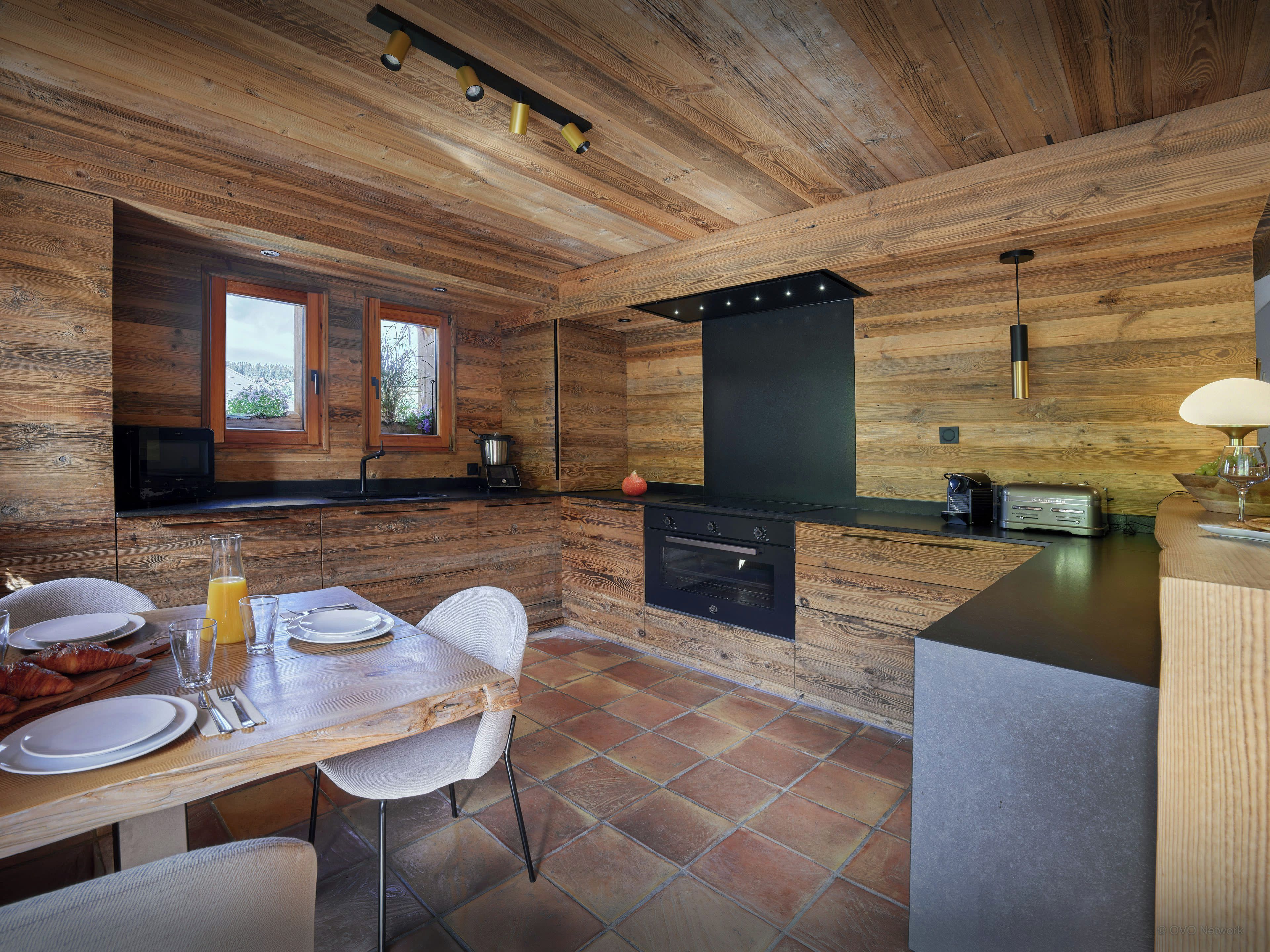Een moderne keuken met houten details, een eethoek met een tafel gedekt voor twee personen, en uitzicht door het raam.