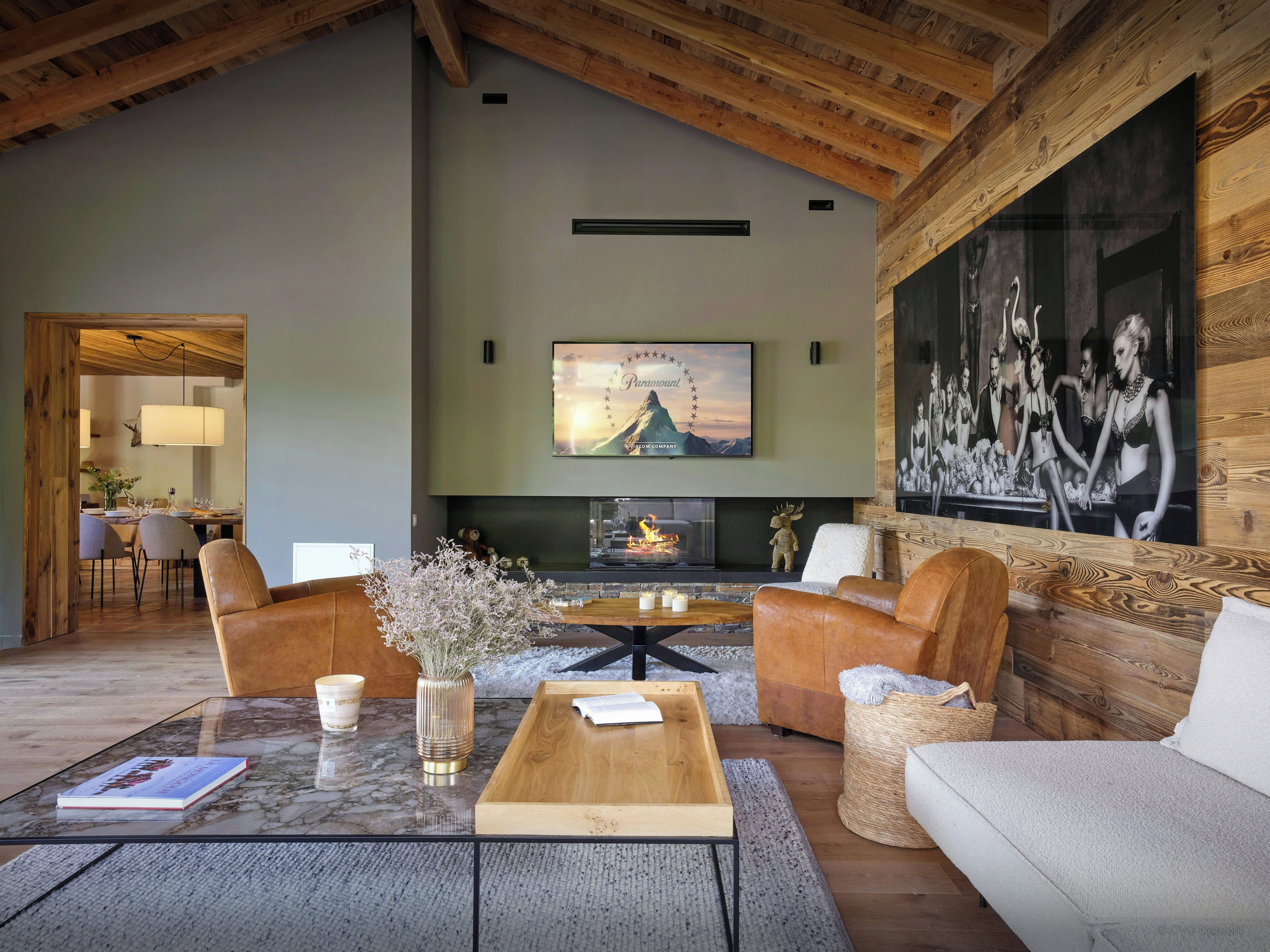 Een ruime woonkamer met een open haard, comfortabele zitmogelijkheden en een grote wandtelevisie.