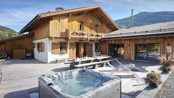 Un chalet in legno con idromassaggio, area salotto esterna e montagne sullo sfondo.