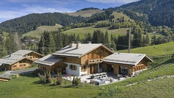 Eine Holzhütte mit Terrasse und Whirlpool, eingebettet in üppige, grüne Hügel unter blauem Himmel.