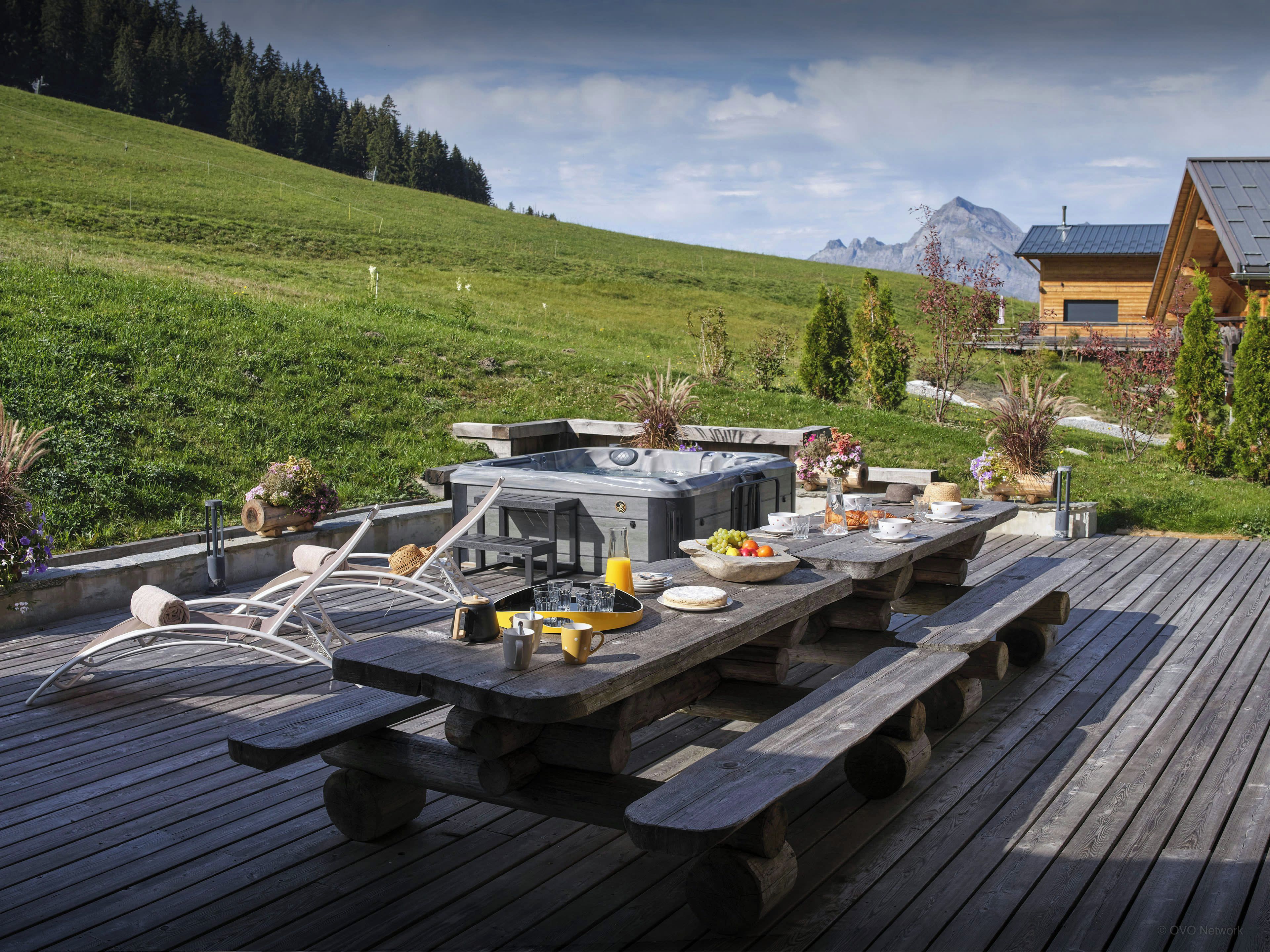 Eine Holzterrasse mit Whirlpool und Esstisch für Mahlzeiten im Freien.