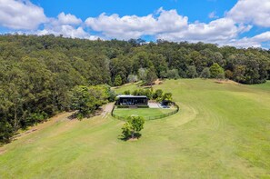 A modern house with a large deck, surrounded by a well-maintained lawn and dense forest. - Gold Leaf Hinterland Stay, Dam & Dog-Friendly (Hinterland Region)