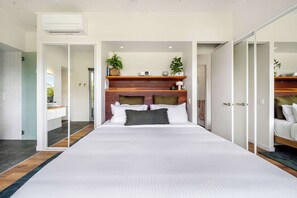 A modern bedroom with a large bed, a wooden headboard, and a built-in shelf with plants and decorative items. - Gold Leaf Hinterland Stay, Dam & Dog-Friendly (Hinterland Region)