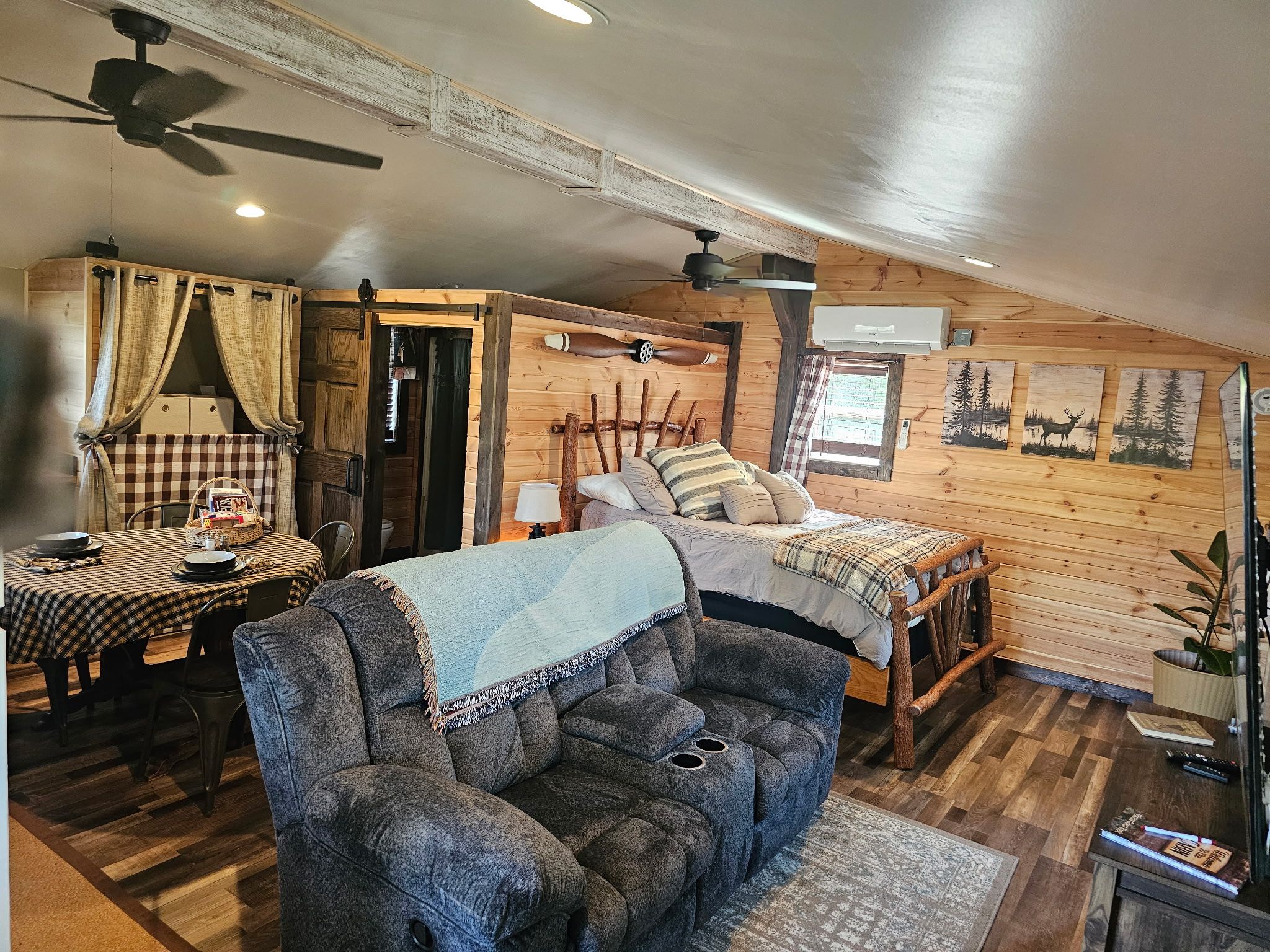 Ein gemütliches Blockhaus-Interieur mit einem Bett, einer Couch, einem Esstisch und einem Deckenventilator.