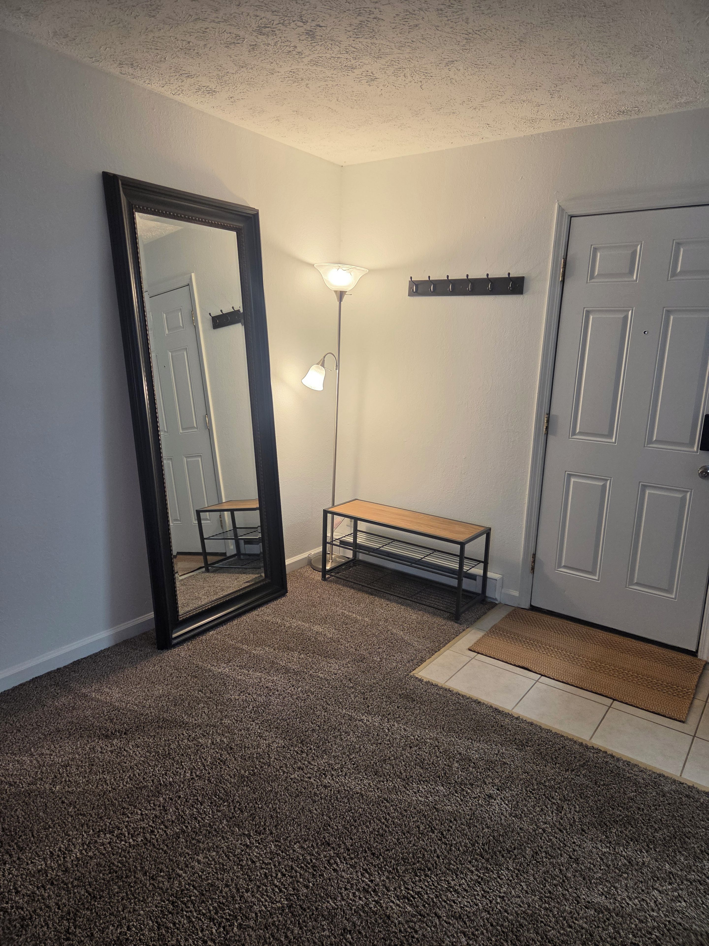 A room with a large mirror, a floor lamp, a bench, and a door.