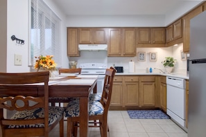 Een moderne keuken met houten kastjes, een witte kookplaat en een eettafel met stoelen.