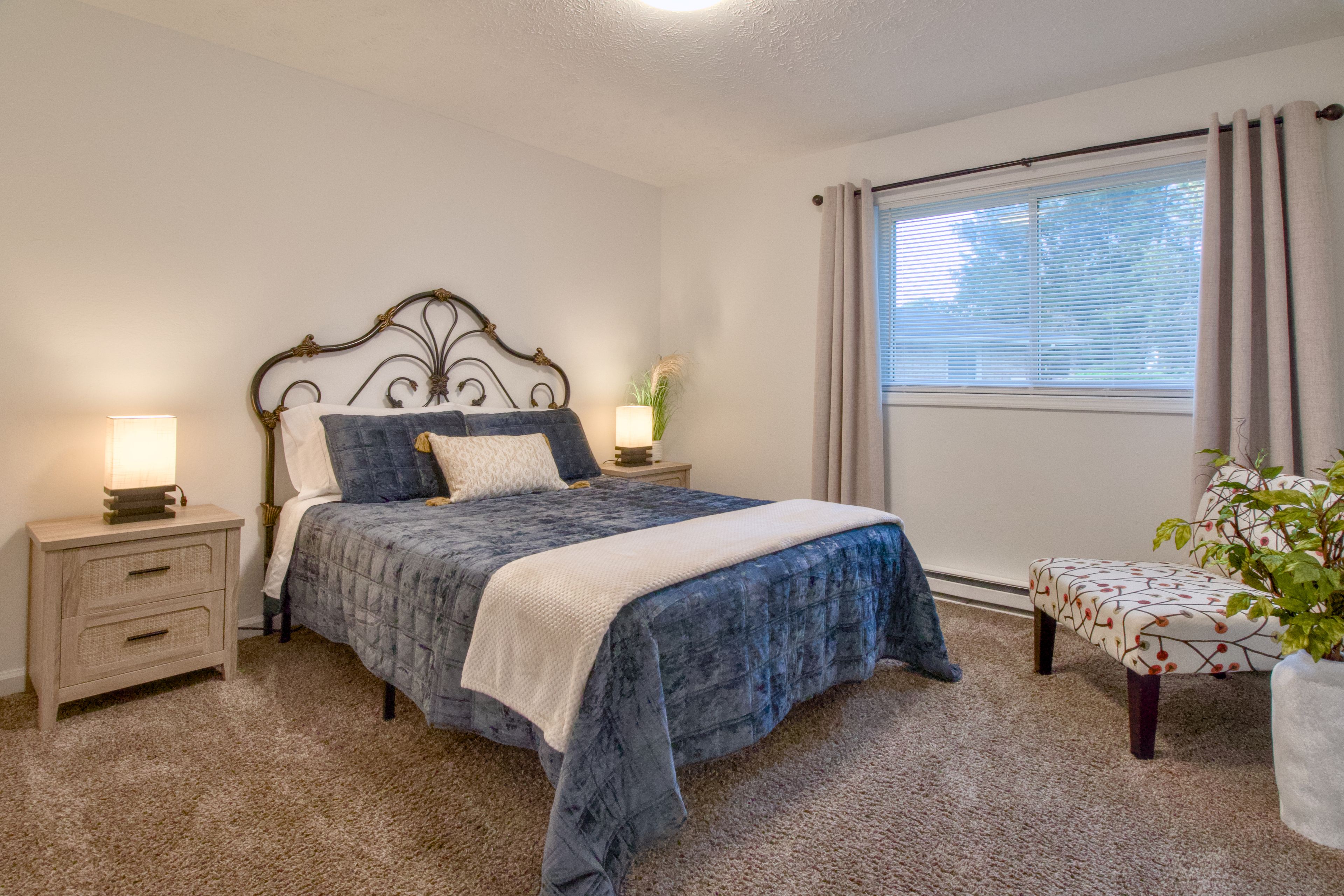 A bedroom with a bed, bedside tables, a window with curtains, and a potted plant.