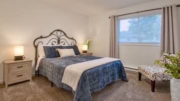 A bedroom with a bed, bedside tables, a window with curtains, and a potted plant.