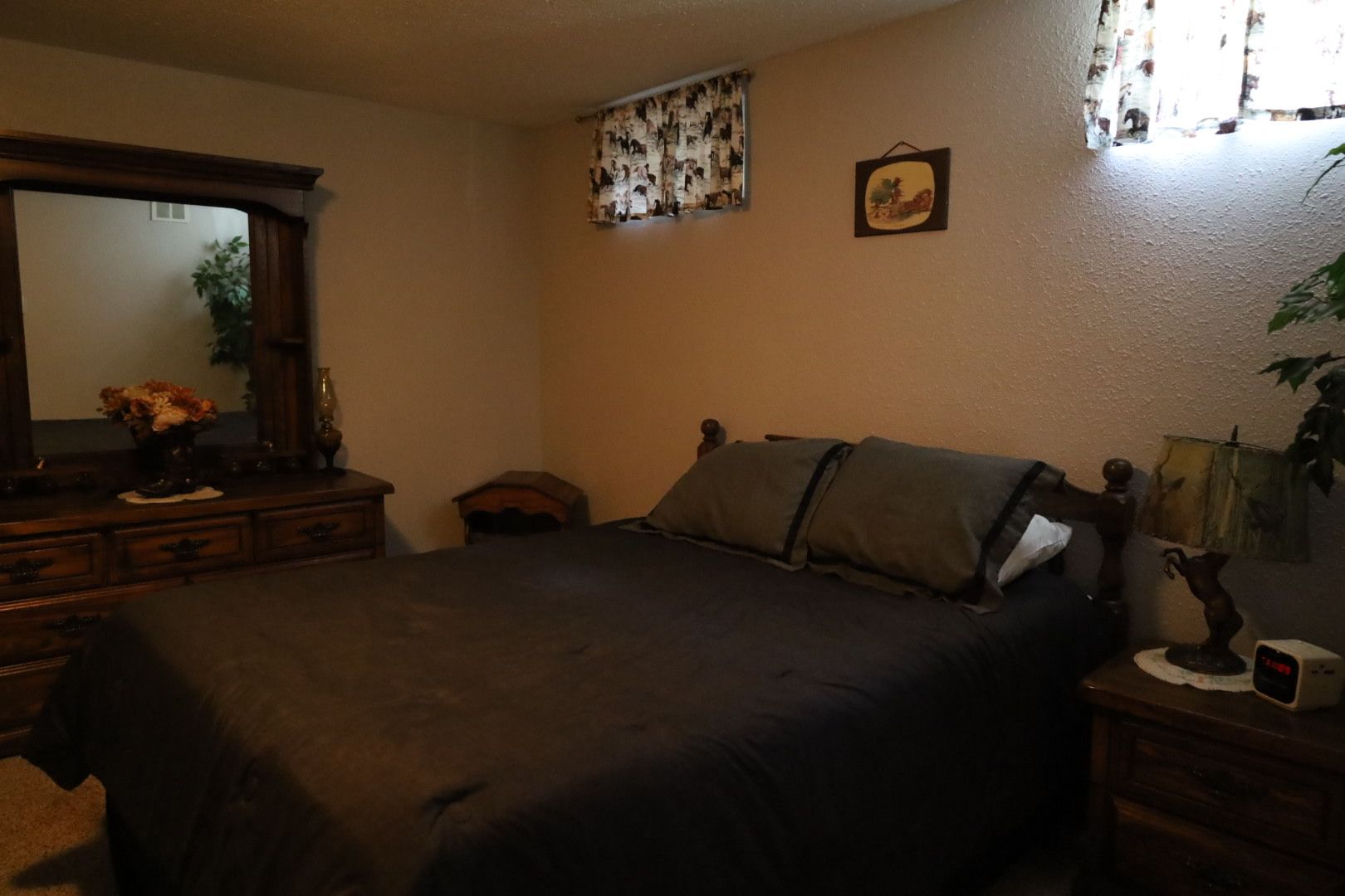 A bedroom with a large bed, a dresser, a mirror, and a small table with a lamp.
