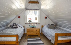 A small, triangular attic bedroom with two beds, a nightstand, a lamp, and a window with curtains. - Nice home in Beddingestrand with house sea view (Beddingestrand)