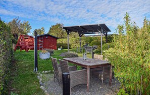 A garden with a wooden table and chairs, a red shed, and a metal structure. - Nice home in Beddingestrand with house sea view (Beddingestrand)