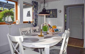A dining area with a round table, white chairs, a hanging pendant light, and a window with a sailboat model. - Nice home in Beddingestrand with house sea view (Beddingestrand)