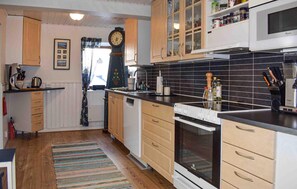 A kitchen with wooden cabinets, a microwave, a stove, and a clock on the wall. - Nice home in Beddingestrand with house sea view (Beddingestrand)