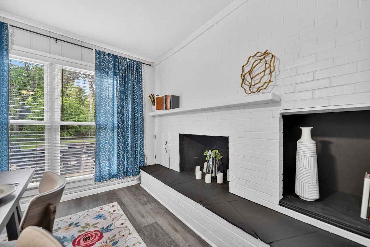A room with a fireplace, a dining area, and a window with curtains.