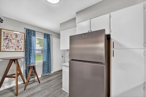 A modern kitchen with white cabinets, a stainless steel refrigerator, and a wooden stool. - Beautiful Brookland / 3BR-2BA / Fire Pit (Lansing)