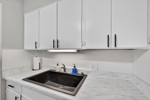 A kitchen with white cabinets, a stainless steel sink, a marble countertop, and a roll of paper towels. - Beautiful Brookland / 3BR-2BA / Fire Pit (Lansing)