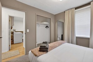Ein Schlafzimmer mit einem Bett, einem Nachttisch mit Handtuch, einem Spiegel und einem Fenster mit Vorhängen.