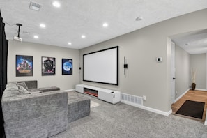 Een bioscoopzaal met een grote flatscreen-televisie, grijze banken en een vloerkleed.