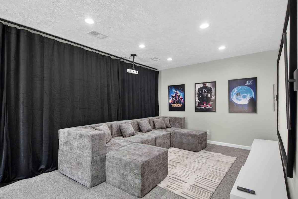A modern living room with a sectional sofa, a flat-screen TV, and three movie posters on the wall.