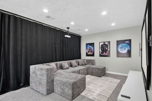Een moderne woonkamer met een modulaire bank, een flatscreen-televisie en drie filmposters aan de muur.