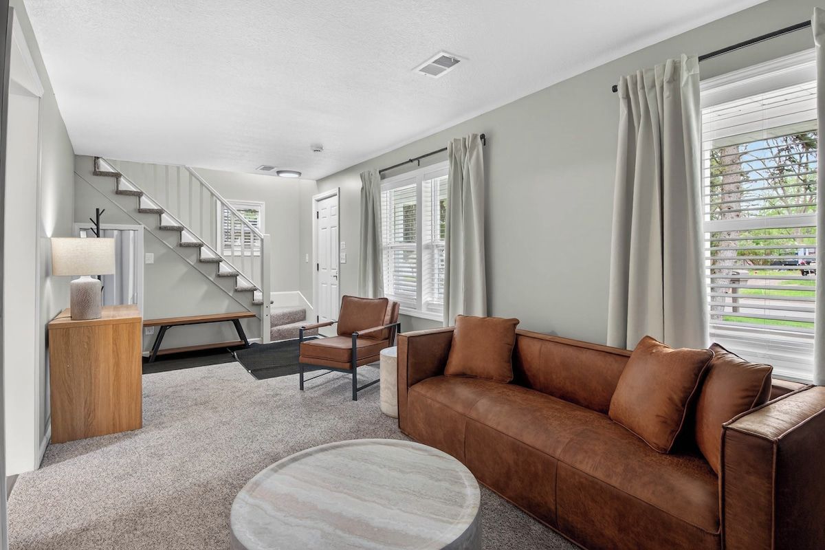 A modern living room with a brown leather sofa, a round coffee table, and a staircase leading to another level.