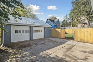 A garage with a white door, a wooden fence, and a driveway leading to a house with a blue roof. - Walk to Sparrow I 2 BR I 1 BA (Lansing)