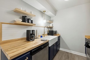 A compact kitchen with a wooden countertop, a built-in dishwasher, a microwave, and a coffee maker. - The Hangar #11 - 2BR - 1BA (Lansing)